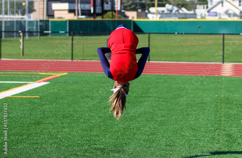 Cheerleader upside down while flipping over a turf field