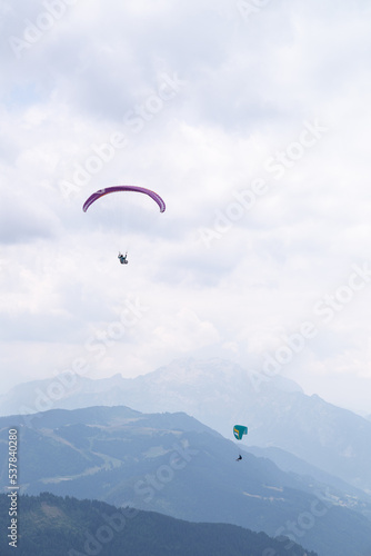 Two paragliders flying over mountains on a cloudy day at french alps. 