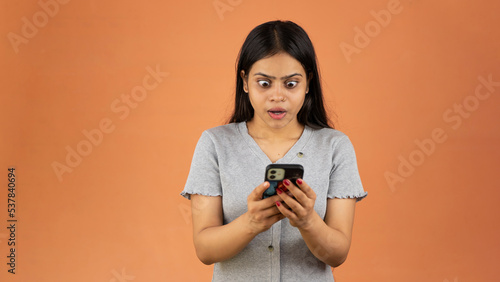 Surprised young woman using mobile phone, shocked face Indian woman holding smartphone, Looking at cell phone screen, isolated over color background