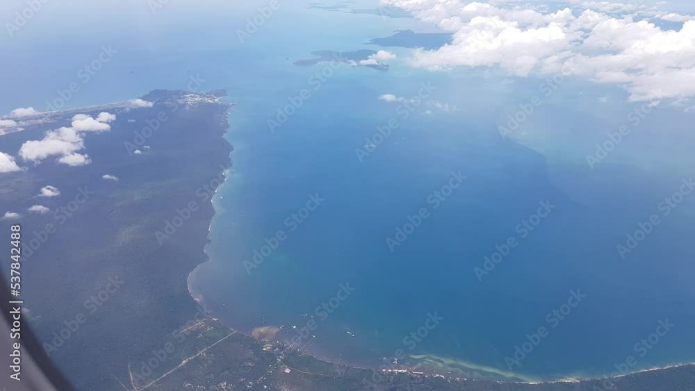 Little window of airplane. Blue sky with clouds and sunshine. Green landscape in below. White wing of aircraft. Glorious sight.