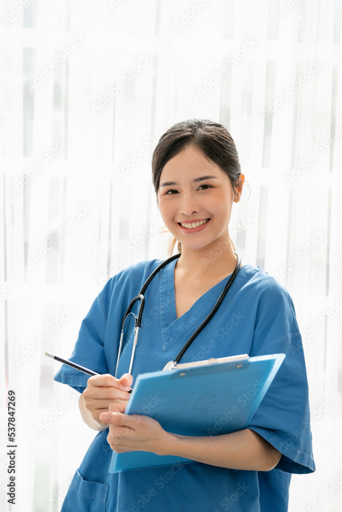 Asian female doctor in blue medical uniform with stethoscope standing and holding a folder, Woman working in a hospital looking at camera and smiling, Medical concept Asian female doctor in blue medical uniform with stethoscope standing and holding a folder, Woman working in a hospital looking at camera and smiling, Medical concept