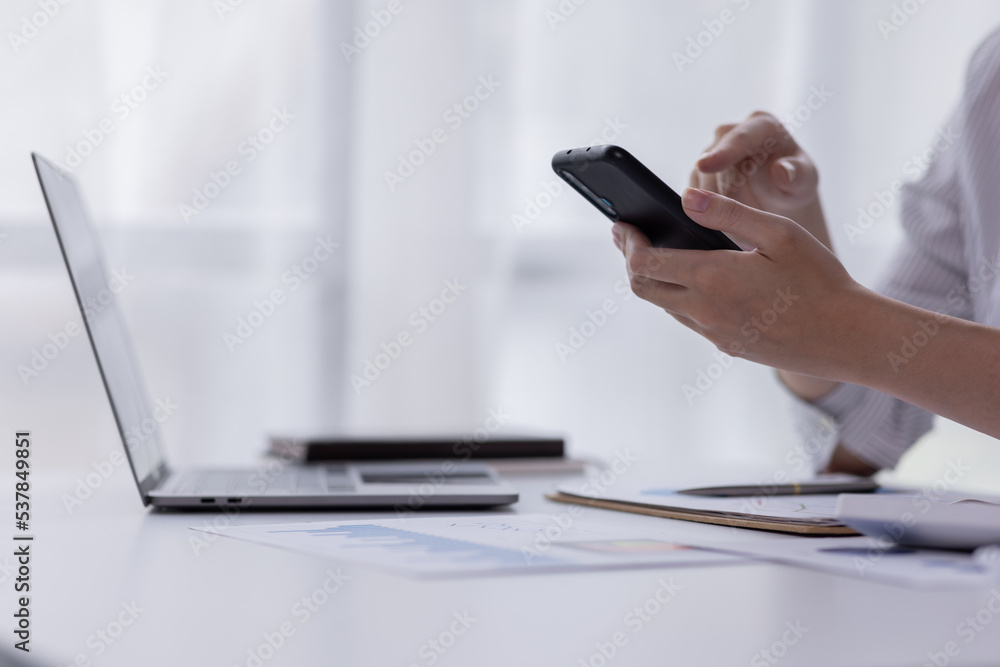 Fototapeta premium Image of smiling attractive and charming asian woman using mobile phone while working on laptop in modern office