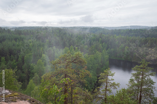 Soft focus image of fog raising over the lake, rocks and forest in the Repovesi National Park after the rain on cloudy summer day. View from Katajavuori Hill