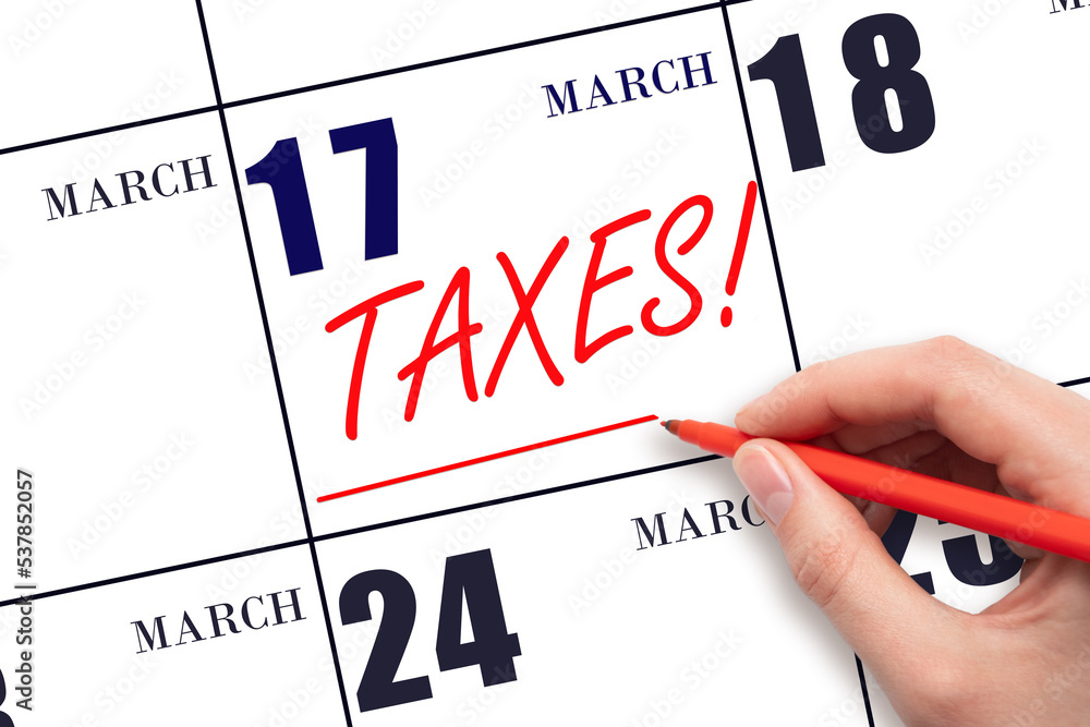 Hand drawing red line and writing the text Taxes on calendar date March 17. Remind date of tax payment Hand drawing red line and writing the text Taxes on calendar date March 17. Remind date of tax payment