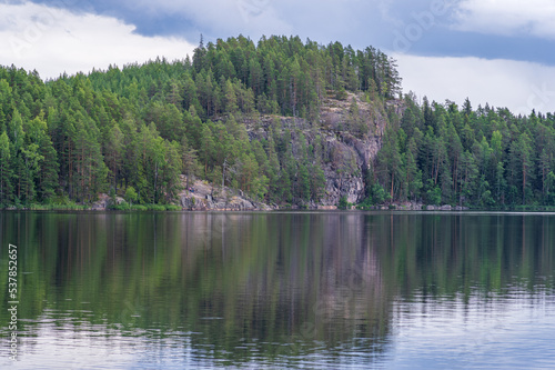 Pine forest growing on cliffs by the lake in Repovesi National park on sunny summer day. Beautiful reflection in the calm water 