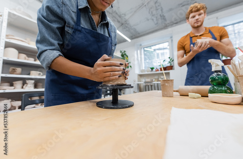 african american woman molding clay cup near blurred and redhead man.