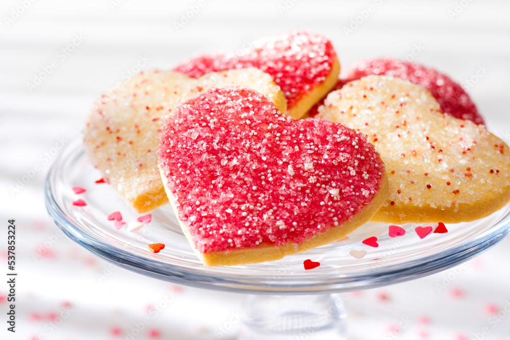 Heart shaped sugar cookies with white, pink, and red sugar sprinkles on a glass tray Heart shaped sugar cookies with white, pink, and red sugar sprinkles on a glass tray