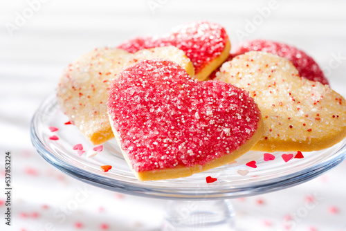 Heart shaped sugar cookies with white, pink, and red sugar sprinkles on a glass tray