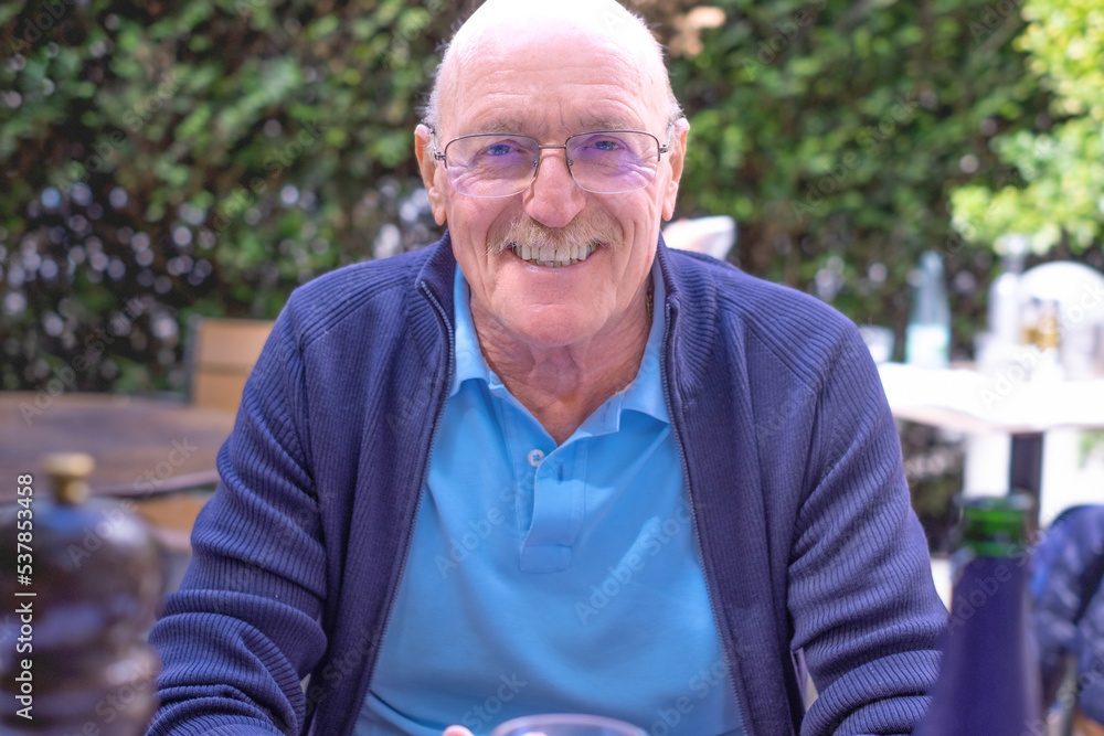 Portrait of beautiful smiling senior man with moustache and eyeglasses sitting in outdoor. Elderly caucasian male looking at camera Portrait of beautiful smiling senior man with moustache and eyeglasses sitting in outdoor. Elderly caucasian male looking at camera