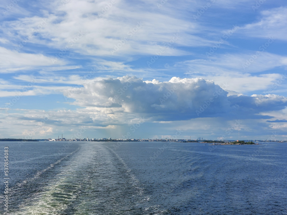 View from the sea to Helsinki skyline on summer evening. Water trail behind ferry in the Baltic sea in the foreground
