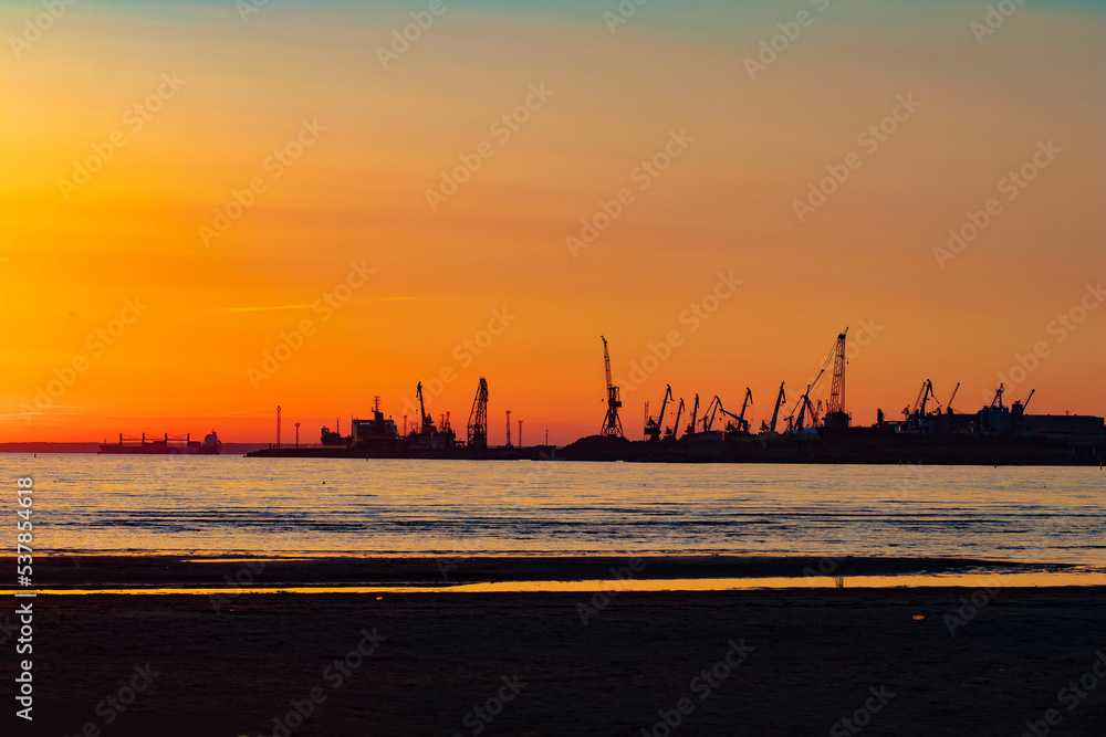 Silhouette of a shipyard with boats and cranes in orange sunset with copy space