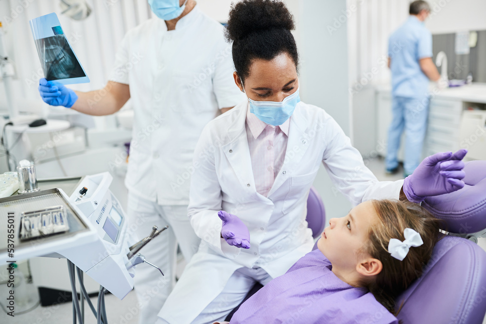 African American female stomatologist communicating with girl at dentist's office.