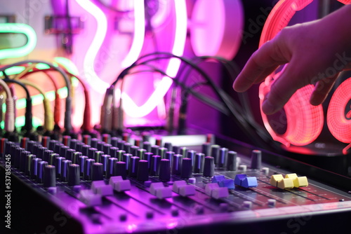 Mixer in home music production studio with hand reaching to operate controls, neon background © Super Retro Digital