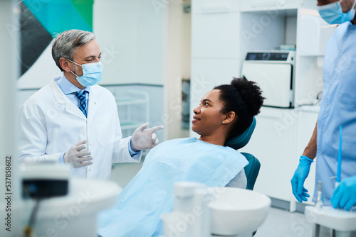 Happy stomatologist talks to black female patient during dental procedure at dentist s office.