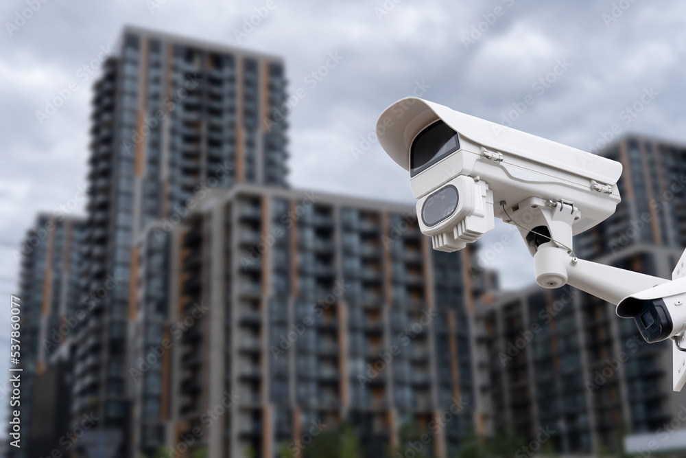 Panoramic view of CCTV surveillance camera with blurred apartment building background with copy space for background banner.