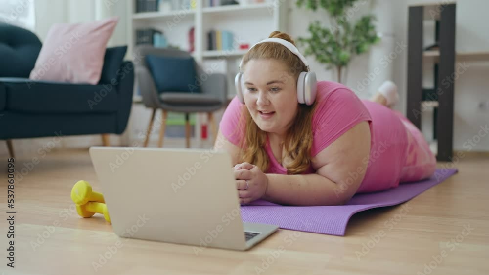 Lazy overweight woman lying on sports mat watching video online instead training Lazy overweight woman lying on sports mat watching video online instead training