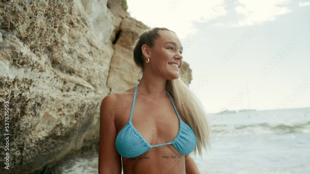 Young European woman in bikini on the beach in summer. Happy young woman smiling at the sea. Tanned blonde girl in swimwear enjoying the beach. Cinematic 4K Young European woman in bikini on the beach in summer. Happy young woman smiling at the sea. Tanned blonde girl in swimwear enjoying the beach. Cinematic 4K