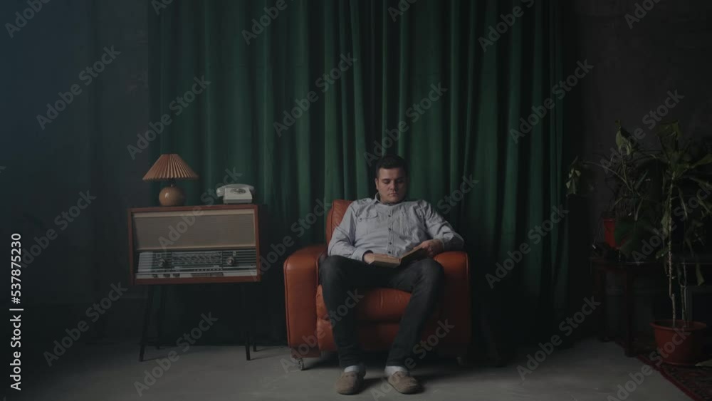 Man sitting in brown armchair and reading the book. Loft room interior.