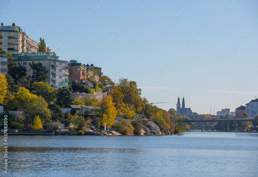 Fototapeta premium Apartment houses on a cliff in the district Kungsholmen, skyline with church towers a sunny a color full autumn day in Stockholm