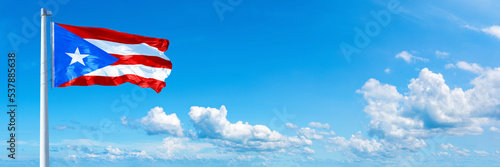 Puerto Rico flag waving on a blue sky in beautiful clouds - Horizontal banner