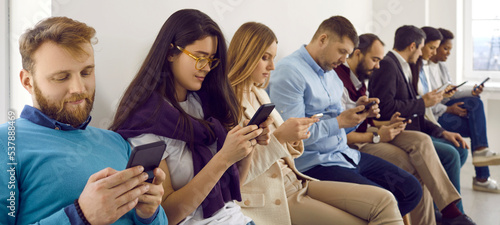 Group of people using modern mobile phones. Male and female millennials sitting in row in office with stable rapid wi fi connection  looking at smartphone screens  text messaging  scrolling news feed