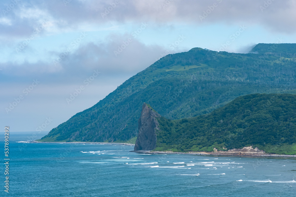 coastline of Kunashir island with basalt cliff and wooded mountains in the clouds