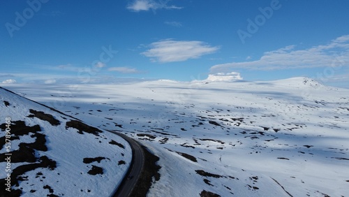 Aerial shot of snow-covered mountains and a curvy road near Valdresflye mountain plateau in Norway photo