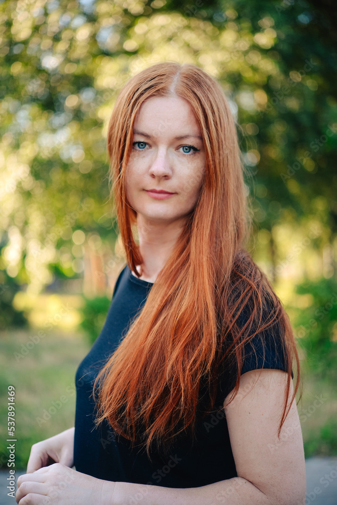 portrait of a beautiful red-haired woman with long hair in a black dress. woman in the park. portrait of a beautiful red-haired woman with long hair in a black dress. woman in the park.