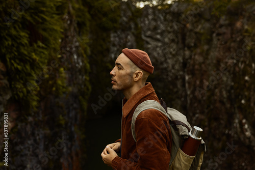 Wallpaper Mural A caucasian man wearing a beanie and a brown jacket with a backpack standing in front of a rock in the forest. Torontodigital.ca