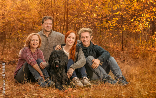 Smiling family with black dog sitting in autumn park