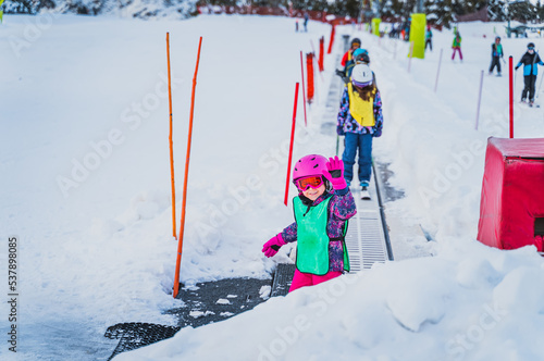 Young skier, girl waving and smiling while going up on ski conveyor. Ski winter holidays in Andorra, El Tarter, Pyrenees Mountains, Grandvalira photo