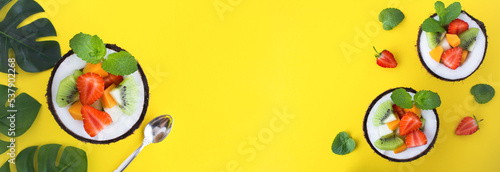 Fruit salad in the half coconut on the yellow background. Banner. Top view.Copy space.
