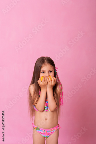Caucasian beautiful little girl with fresh yellow lemons on a pink background. Little girl with lemon. Funny child isolated on pink.