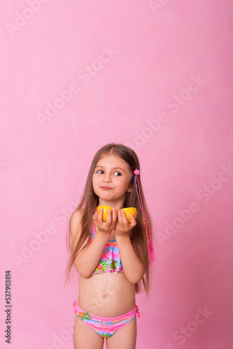 Caucasian beautiful little girl with fresh yellow lemons on a pink background. Little girl with lemon. Funny child isolated on pink.