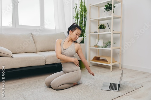 Young Asian woman in front of her laptop doing sports and yoga repeating exercises on video at home  home workout complex for body twisting lifestyle