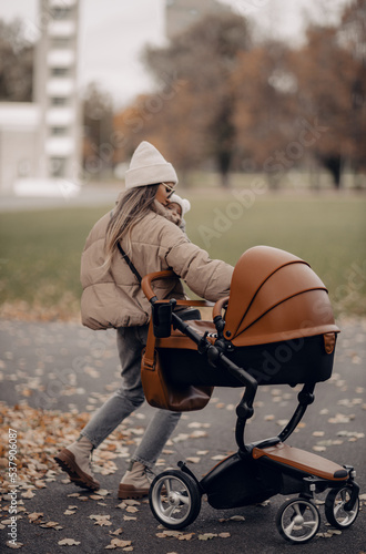 Happy family outdoors, a young stylish fashion mother holding baby near stroller in the autumn on nature. photo