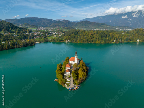 Famous alpine Bled lake (Blejsko jezero) in Slovenia, amazing autumn landscape. Scenic view of the lake, island with church, mountains and blue sky with clouds, outdoor travel background from drone