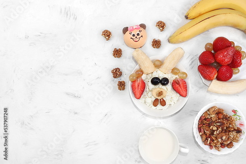 Healthy breakfast with ingredients, fun food for kids. The concept of healthy and natural food. Oatmeal or cottage cheese with muesli, banana and strawberries, nuts and cookies, top view,