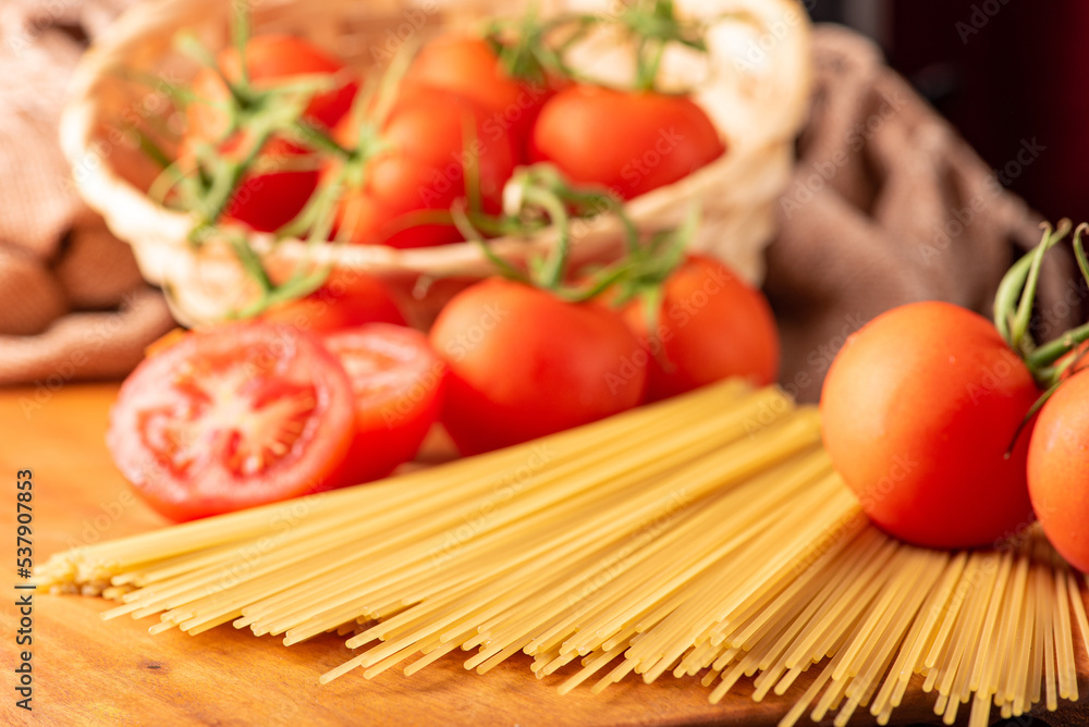 Pasta, beautiful details of red tomatoes and strands of raw spaghetti over rustic wood, selective focus. Pasta, beautiful details of red tomatoes and strands of raw spaghetti over rustic wood, selective focus.