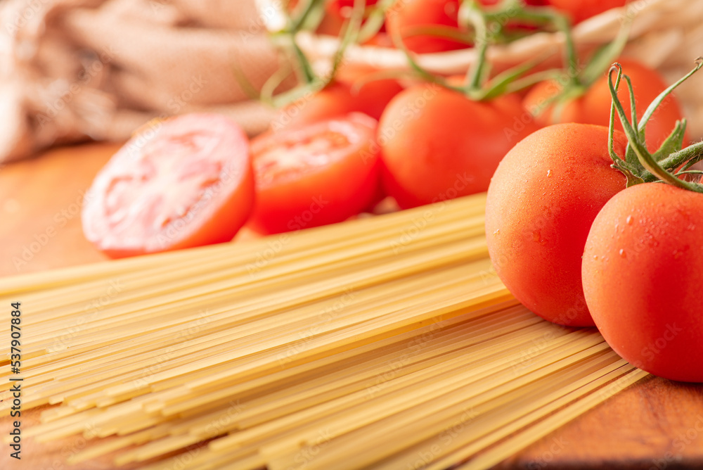 Pasta, beautiful details of red tomatoes and strands of raw spaghetti over rustic wood, selective focus. Pasta, beautiful details of red tomatoes and strands of raw spaghetti over rustic wood, selective focus.