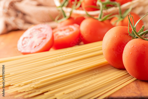 Pasta, beautiful details of red tomatoes and strands of raw spaghetti over rustic wood, selective focus.