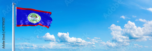 Belize flag waving on a blue sky in beautiful clouds - Horizontal banner