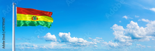 Bolivia flag waving on a blue sky in beautiful clouds - Horizontal banner photo