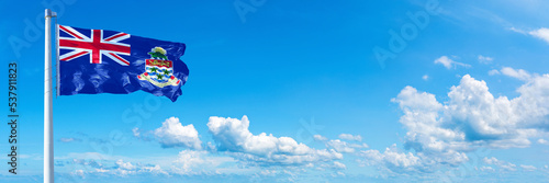 Cayman Islands flag waving on a blue sky in beautiful clouds - Horizontal banner