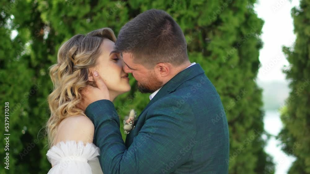 the bride and groom kiss and hugging in the park. 