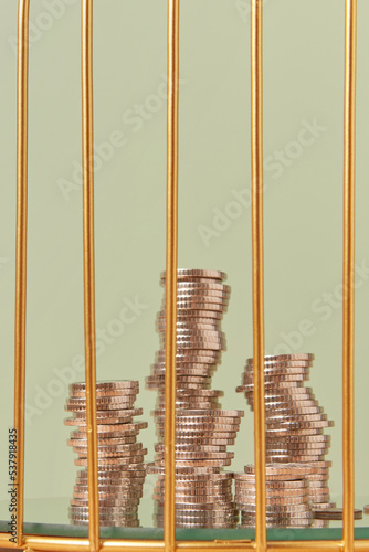Cent coins stacks behind golden cage bars.