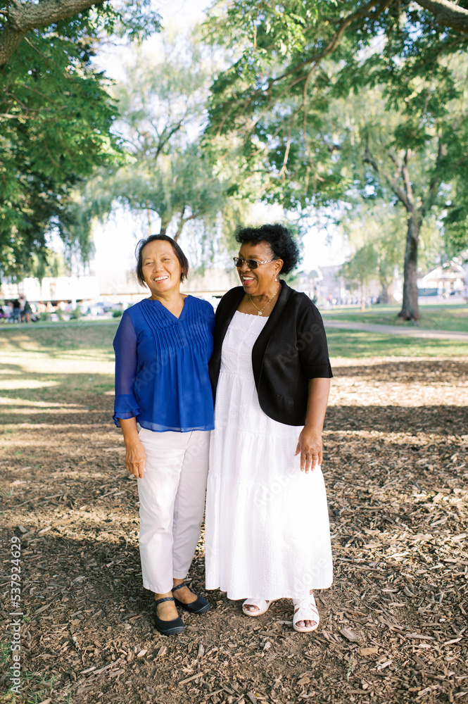 Two senior women standing together under a tree in a park Two senior women standing together under a tree in a park