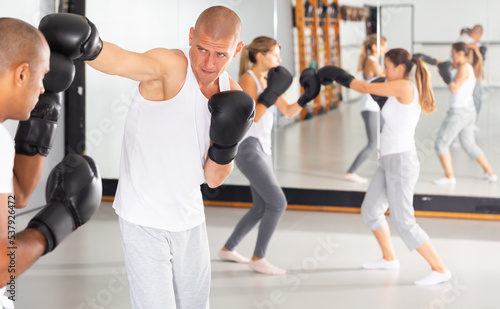 Emotional adult man mastering self defense techniques, practicing punches during sparring in training room