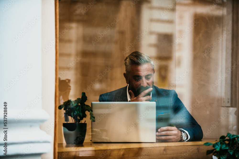 Modern senior businessman sitting in cafe and using laptop and smartphone Modern senior businessman sitting in cafe and using laptop and smartphone