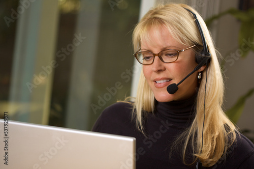 Foto Attractive Businesswoman Wearing Phone Headset Using a Computer